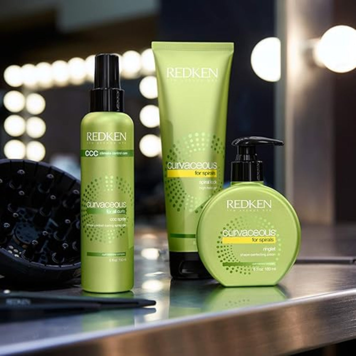 Redken hair care products on a reflective surface with blurred lights in the background